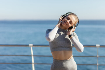 Wall Mural - Slim caucasian fit woman listening to music with headphones at bright sunny day on the beach