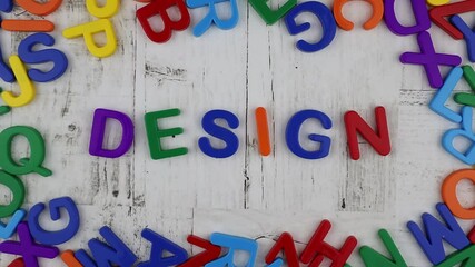 Fototapete - Word - Design - in multicolored alphabet letters centered with frame on a grey wood background viewed in a flat lay still life. Stop motion, top view