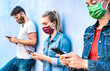 © Mirko Vitali - Milenial friends using mobile phone covered by face mask - Young people sharing content on cellphone - New normal concept about always connected teenager - Vivid azure filter with focus on right hands