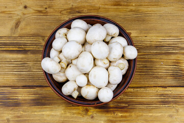 Sticker - Fresh champignon mushrooms in ceramic bowl on the wooden table. Top view