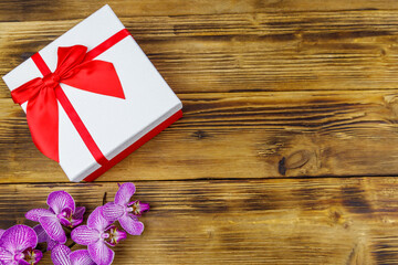 Gift box and orchid flower on a wooden background. Top view, copy space