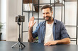 Behind the scenes of young bearded hipster male blogger vlogger streaming video online or recording tutorial for social media network, waving, greeting friends followers with high-five, saying hello
