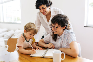 Wall Mural - Female couple looking at their son scribbling in a book