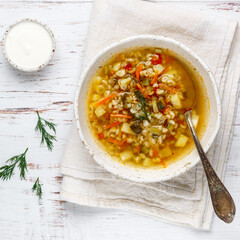 Wall Mural - Thick hearty Pickle soup with vegetables (pickles, cucumbers, carrots, onions, potatoes, tomatoes) and pearl barley in a white plate on a wooden table. Rassolnik. Russian cuisine.  square picture