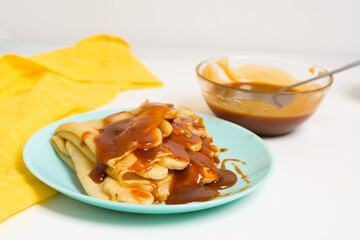 Wall Mural - blini pancakes with caramel, dripping on a spoon levitation close-up on a blue plate on a light background . traditional Russian holiday is a symbol of spring and sweet dessert