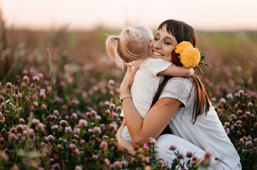 happy family, mother and child daughter are hugging on a flower meadow in summer nature at sunset ti