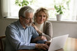 © fizkes - Happy confident mature family couple using app on computer at home. Senior husband and wife typing on laptop, checking bank account or finance insurance balance, shopping, reading or booking online