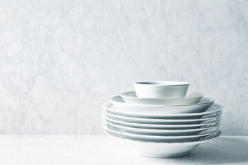 Stack of white porcelain plates and bowls on bright stone background. copy space