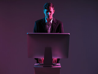 Poster - Man works at a computer while standing. A monitor stand next to man. Businessman and computer on a dark background. A man in a business suit. He is typing something. Concept business management