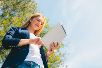 Young caucasian girl with wireless headphones in the park using tablet and smiling