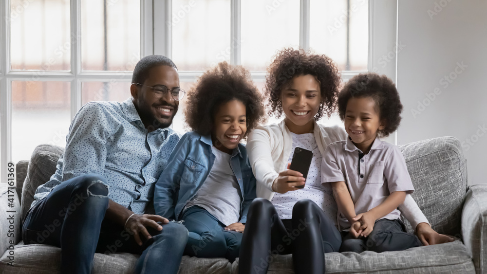 Happy millennial parents and children using smartphone for video or conference call. Black couple and kids talking to family members online or taking selfie together. Distance communication concept