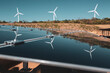 © EZ PHOTOS - Solar panels under a beautiful blue sky reflecting windmills of an eolic windfarm. Renewable energy generation for environmental conservation concept.