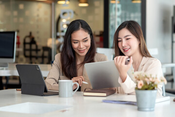 Wall Mural - Two young asian woman discuss concept work at the office using a tablet.