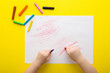 © fotoduets - Baby hands holding wax crayons and drawing first scratches lines on white paper on bright yellow table background. Closeup. Toddler development. Point of view shot. Top down view.