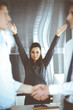 © Iryna - Happy and excited business woman raising hands because of success agreement at meeting. Two men shaking hands in office