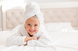 © КРИСТИНА Игумнова - little smiling girl in a white robe with a white towel on her head is lying in bed. portrait of a child