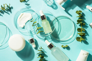Fototapete - Cosmetic laboratory concept . Glass petri dish with cosmetic products, serum bottles, cream, tonic and green leaves at blue background.