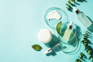 Poster - Cosmetic laboratory concept . Glass petri dish with cosmetic products and serum bottles at blue background. Flat lay image with copy space.
