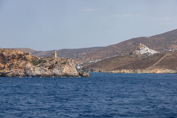 Lighthouse on the rock in the background. Chora , Ios Island, Greece.