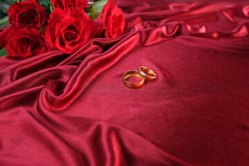 Wall Mural - texture of luxury red silk fabric, background with waves and drapery for fashion design, gold wedding rings. bouquet of roses, concept of congratulations on wedding day