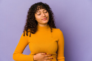 Poster - Young african american afro woman isolated touches tummy, smiles gently, eating and satisfaction concept.