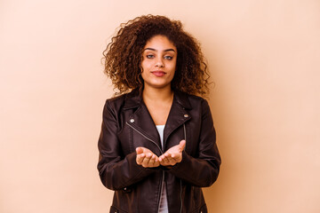 Wall Mural - Young african american woman isolated on beige background holding something with palms, offering to camera.