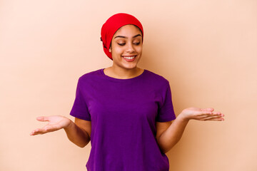 Wall Mural - Young african american woman isolated on beige background holding something with palms, offering to camera.