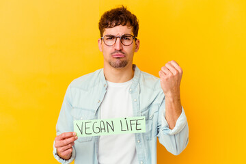 Wall Mural - Young caucasian man holding a vegan life placard isolated showing fist to camera, aggressive facial expression.