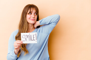 Wall Mural - Young caucasian woman holding a Smile placard isolated touching back of head, thinking and making a choice.