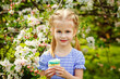 © Elena  - A child in a blooming apple orchard enjoys a warm spring day. The girl holds a cake in her hands, wants to eat it.