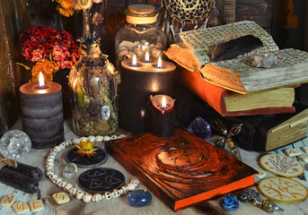 Still life with grimoire book of spells, burning candles, runes and ritual objects on witch table.