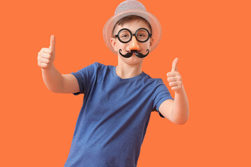 Little boy in funny disguise showing thumb-up gesture on color background. April Fools Day celebration