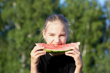 Pretty young girl eating red juicy watermelon in green park background