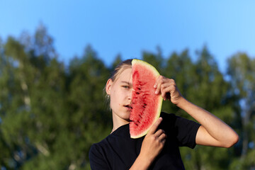 Portrait of pretty teen girl holding slice of watermelon in front of face on green nature background.