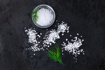 Wall Mural - Coarse salt crystals on a black table. Bowl with sea salt. Background for advertising salty.