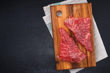 Raw steak on a cutting board with rosemary and spices, dark black background, top view. Fresh grilled meat. Grilled beef steak.