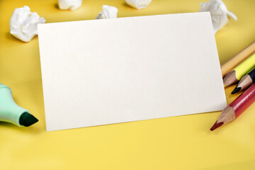 White blank sheet on a yellow background among pencils and markers