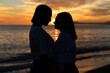 © cocopicfotografia - Joven pareja lesbiana mirándose bajo un atardecer a través de una silueta oscura con precioso mar y fondo de nubes con sol