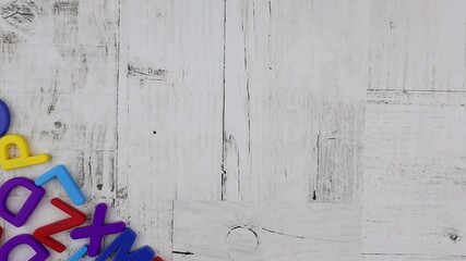 Fototapete - Brightly colored alphabet letters spelling word - White - arranged diagonally above a corner decoration of random colorful letters on a white wood background with copyspace. Stop motion, top view