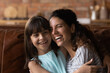 Leinwandbild Motiv Overjoyed young Hispanic mother and little 8s daughter hug have fun playing together in living room. Smiling Latino mom and small girl child relax rest at home, engaged in funny activity on weekend.