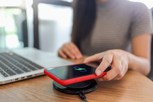 Charging Mobile Phone Battery With Wireless Charging Device In The Table. Smartphone Charging On A Charging Pad. Mobile Phone Near Wireless Charger Modern Lifestyle Concept.
