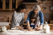 © fizkes - Smiling three generations of Hispanic women have fun baking together with dough at home kitchen. Happy little Latino girl child with young mom and senior grandmother cook pastries or cookies.