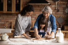 Smiling Three Generations Of Hispanic Women Have Fun Baking Together With Dough At Home Kitchen. Happy Little Latino Girl Child With Young Mom And Senior Grandmother Cook Pastries Or Cookies.