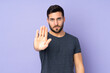 © luismolinero - Caucasian handsome man making stop gesture over isolated purple background