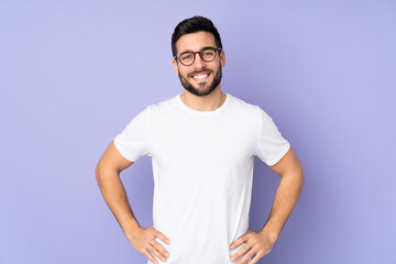 Wall Mural - Caucasian handsome man over isolated background posing with arms at hip and smiling