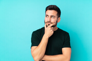 Sticker - Caucasian handsome man isolated on blue background having doubts and with confuse face expression