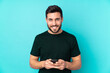 © luismolinero - Caucasian handsome man isolated on blue background sending a message with the mobile