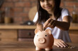 Crop close up of provident economical small girl kid put money into piggybank saving for future needs. Happy smart little 9s teen child make donation contribution in piggy bank. Investment concept.