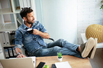 Wall Mural - Young businessman working on laptop and drinking coffee in his office. Businessman on coffee break