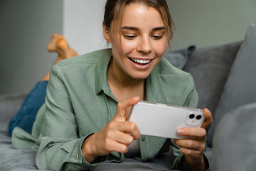 Wall Mural - Happy nice woman using mobile phone while lying on sofa